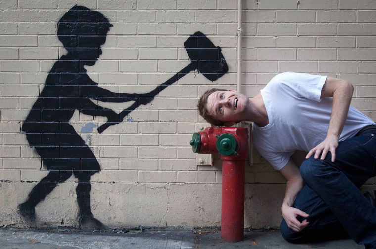 A man jokingly poses with work by British graffiti artist Banksy in New York, Oct. 20, 2013.