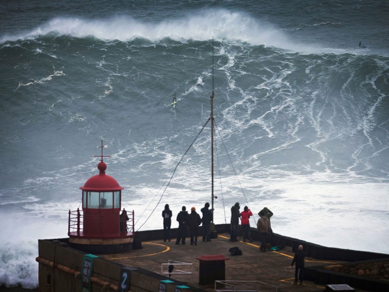 People watch an unidentified surfer ride a big wave at the Praia do Norte, north beach, at the fishing village of Nazare in Portugal's Atlantic coast ...