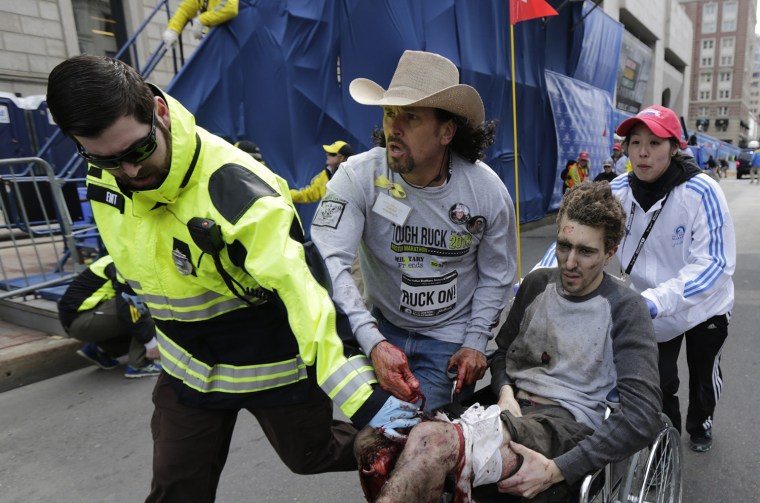 An emergency responder and volunteers, including Carlos Arredondo in the cowboy hat, push Jeff Bauman in a wheel chair after he was injured in an explosion near the finish line of the Boston Marathon Monday, April 15, 2013 in Boston.