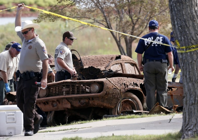 Law enforcement officials from multiple agencies examine the two cars pulled from Foss Lake, in Foss, Okla., on Sept. 18. The Oklahoma State Medical Examiner's Office says authorities have recovered skeletal remains of multiple bodies in the Oklahoma lake where the cars were recovered.