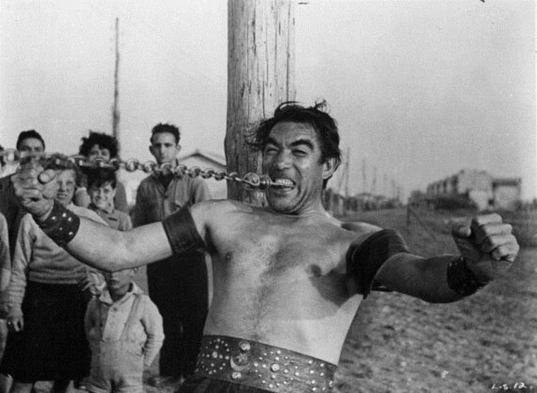 Anthony Quinn continues to bite down on a metal chain as he pulls it away from him in a scene from the film 'La Strada', 1954.