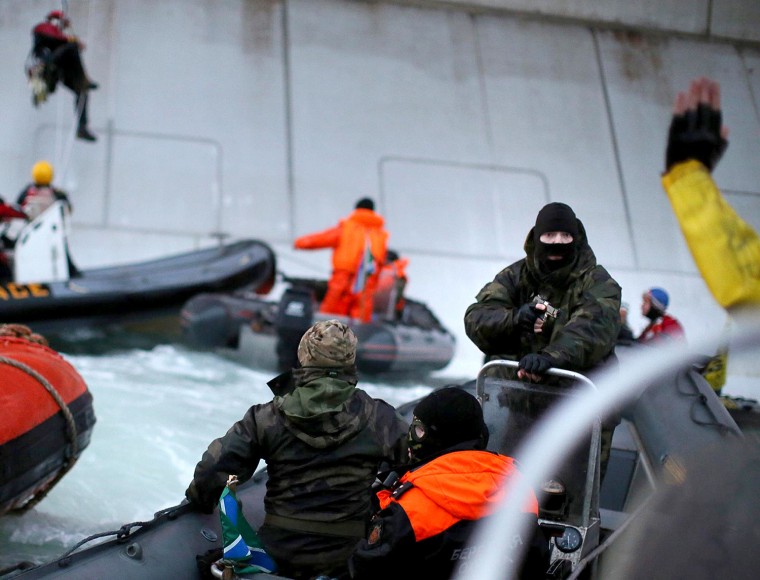 A handout photo taken by Greenpeace on September 18, 2013, shows a camouflage clad mask wearing officer of Russian Coast Guard pointing a gun at a Greenpeace International activist during the environmentalists' attempt to climb Gazproms Prirazlomnaya Arctic oil platform.