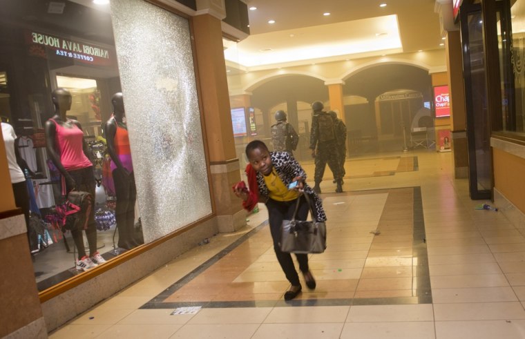 A woman who had been hiding during the gun battle runs for cover after armed police, seen behind, enter the Westgate mall in Nairobi, Kenya, on Saturday. The Somalia-based terrorist group al-Shabab claimed responsibility for the attack.