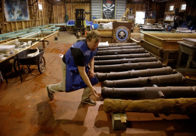 Chris Macort, a field archeologist working with the Whydah pirate ship museum, reaches down to check one of the ships cannons at the museum's warehouse in Brewster, Mass.