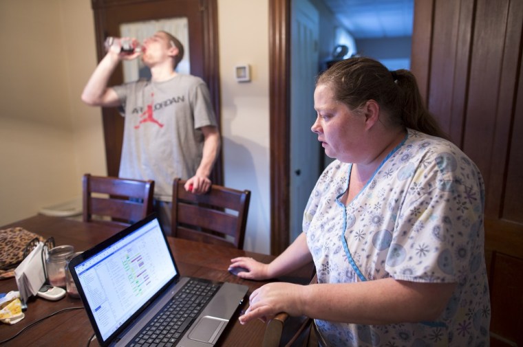 Anne Leone works at the kitchen table in her Auburn, NY home while her daughter's boyfriend, Bobby Kindred Jr., chugs a soda.