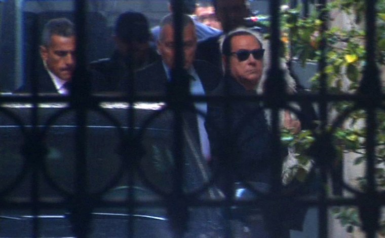 Silvio Berlusconi carries his pet dog as he arrives at his home in Rome in this image taken from video on Monday.