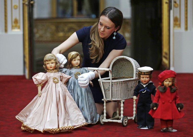 Exhibition curator Anna Reynolds poses with dolls and a wicker toy pram belonging to Britain's Queen Elizabeth and her sister Princess Margaret, at Bu...