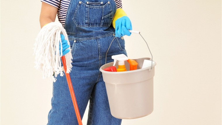 Woman in overalls holding a bucket full of cleaning supplies and mop