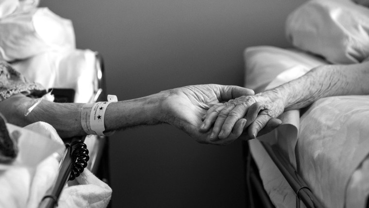 In this July, 2014 photo provided by their granddaughter Melissa Stone, Don Simpson, 90, and his wife Maxine, 87, hold hands from adjoining hospice be...