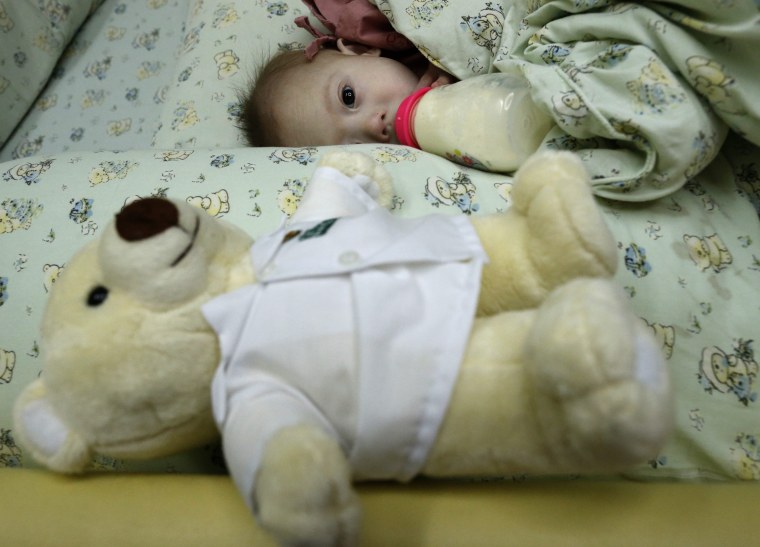 epa04340368 A Thai seven-month-old Down's Syndrome surrogate baby, Gammy or Naruebet Mincharoen drinks from a bottle of milk next to his Teddy bear at...