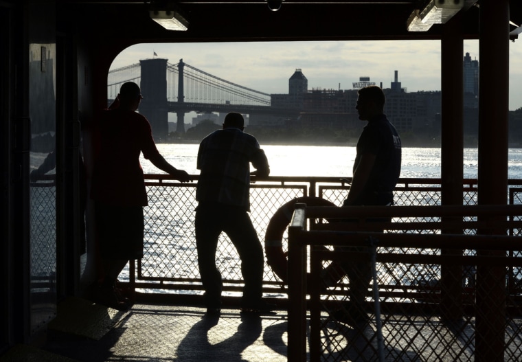 With the Brooklyn Bridge in the background, passengers on the Staten Island Ferry watch the morning sunrise on July 11, 2014, in New York Harbor.