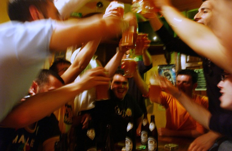 Men toast with glasses of beer in a pub.