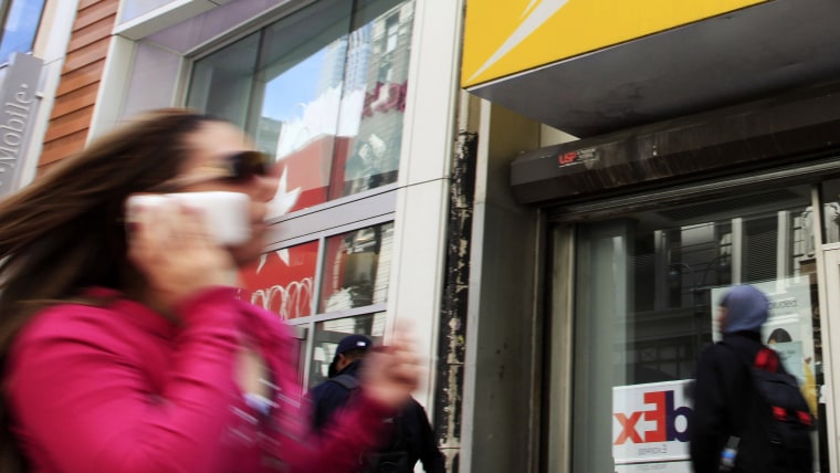 A woman using a cell phone walks past T-Mobile and Sprint stores, Tuesday, April 27, 2010, in New York. Sprint Nextel Corp. on Wednesday, April 28, sa...