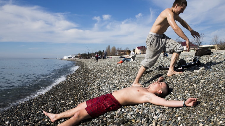 People enjoy the sunny weather at the Black Sea beach with the Fisht Stadium (rear) in the Olympic Park visible in the background, Sochi, ...