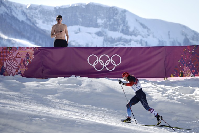 A shirtless spectator watches Russia's Julia Ivanova compete during the women's 10K classical-style cross-country race at the 2014 Winter Olympics, Th...