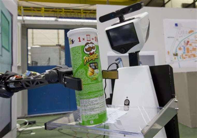 A robotic arm, left, puts a package of Pringles on the serving tray of another robot to deliver it to an imaginary patient in a mock hospital room at ...
