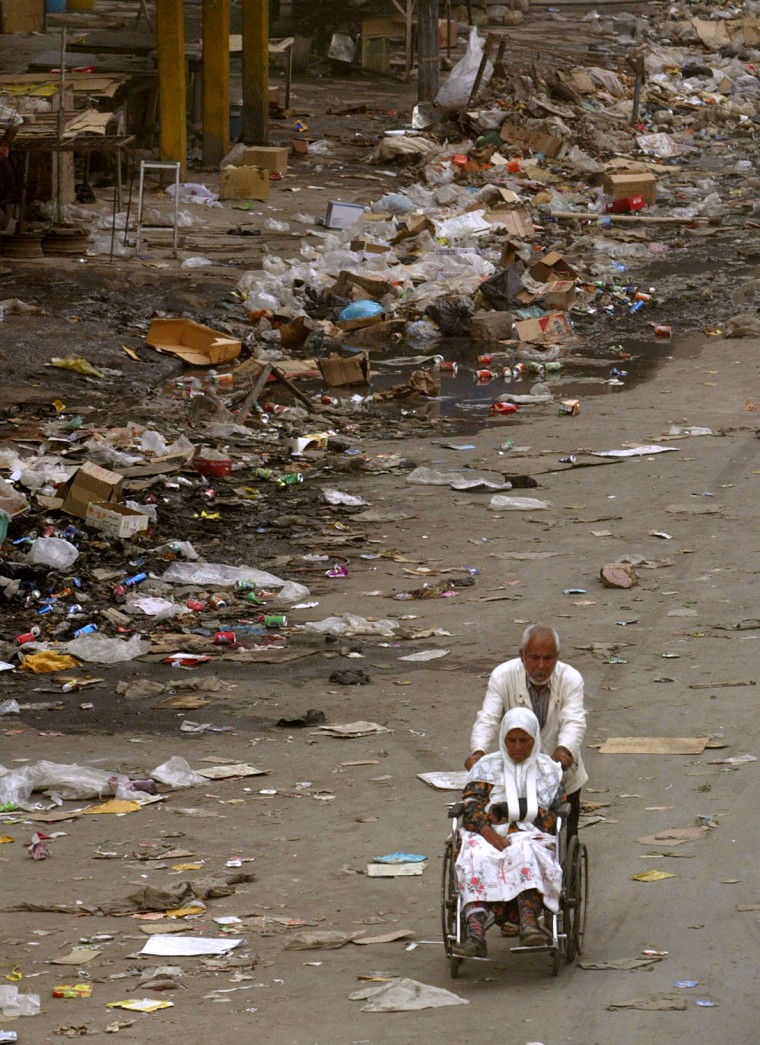 An Iraqi man pushes a woman in a wheelchair past piles of trash in Baghdad in May, 2003.