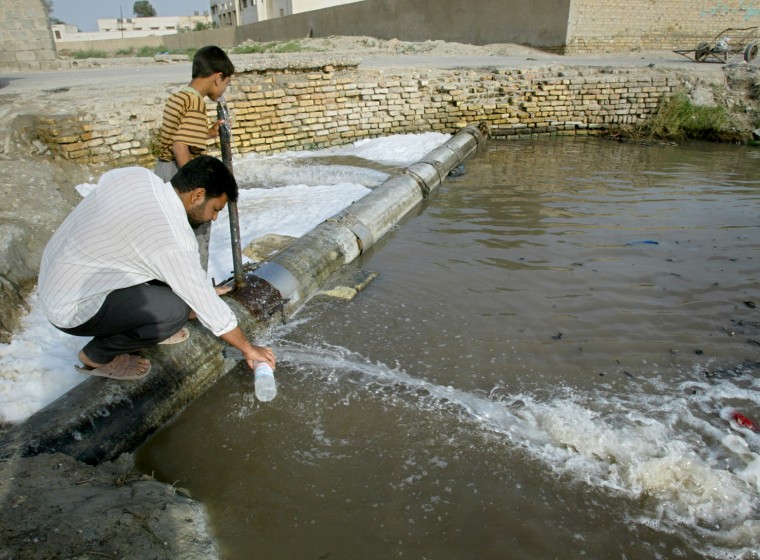 An Iraqi man fills a plastic bottle with drinking water from a leaking pipe as his son drinks in Basra, May 8, 2003.