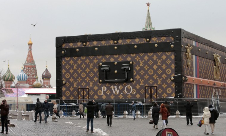 People walk past a Louis Vuitton pavilion which is in the shape of a giant suitcase, as the St. Basil's Cathedral and the Spasskaya Tower are seen in the background, in central Moscow, November 27, 2013.