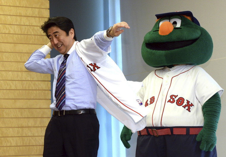 Japan's Prime Minister Shinzo Abe smiles as he puts on a Boston Red Sox jersey, while Red Sox mascot Wally looks on.