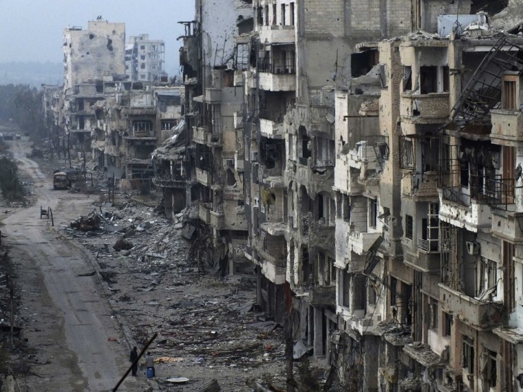 People stand on a street lined with damaged buildings in the besieged area of Homs January 27, 2014.