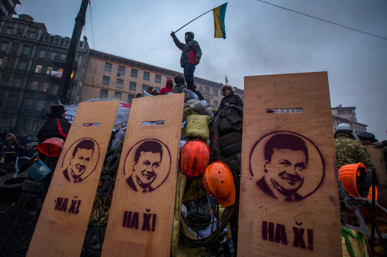 An anti-government protester waves the Ukrainian flag as he stands on fortifications against riot police in Kiev on Tuesday.