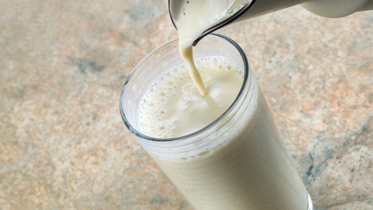 Pitcher pouring almond milk into glass with stone counter top in background