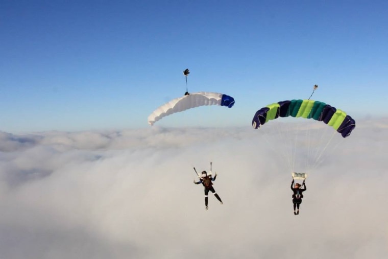 Amy Olson and Chad Ebling in air wearing parachutes.