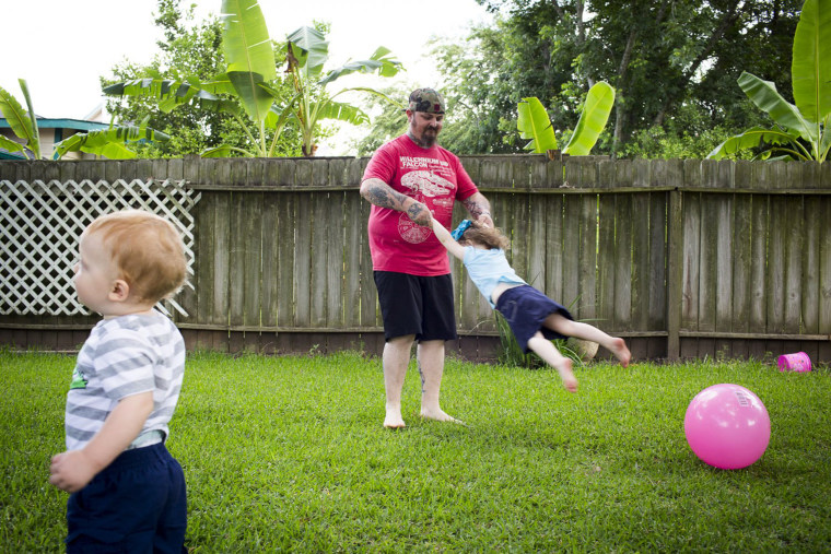 Image: Lance Stewart swings around his daughter Brooklyn, 3, while his son Connor, 1, wanders by at their home in League City, Texas.
