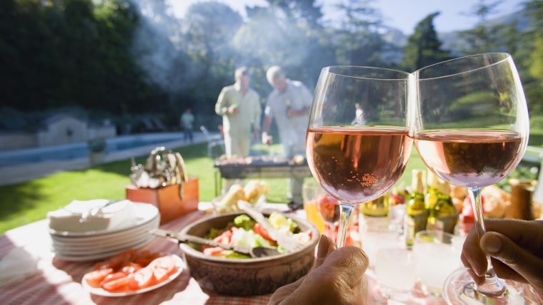 Men grilling food at family barbecue in summer garden, focus on food and wine on table in foreground