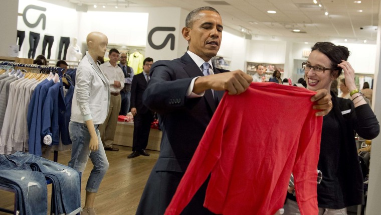 US President Barack Obama holds up a shirt as he shops for clothing for his family alongside store employee Susan Panariello (R) during a visit to a G...