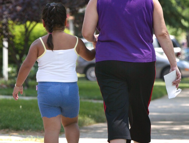 A young girl walks with her mother along a sidewalk.