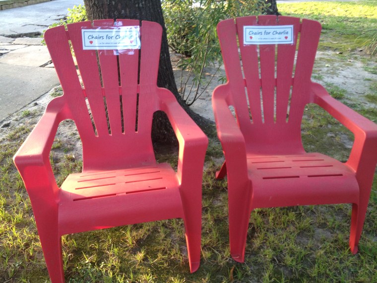 Two red Adirondack chairs with signs that say: Chairs for Charlie. They are for Charlie George, who is battling leukemia, to use as he strolls the neighborhood.