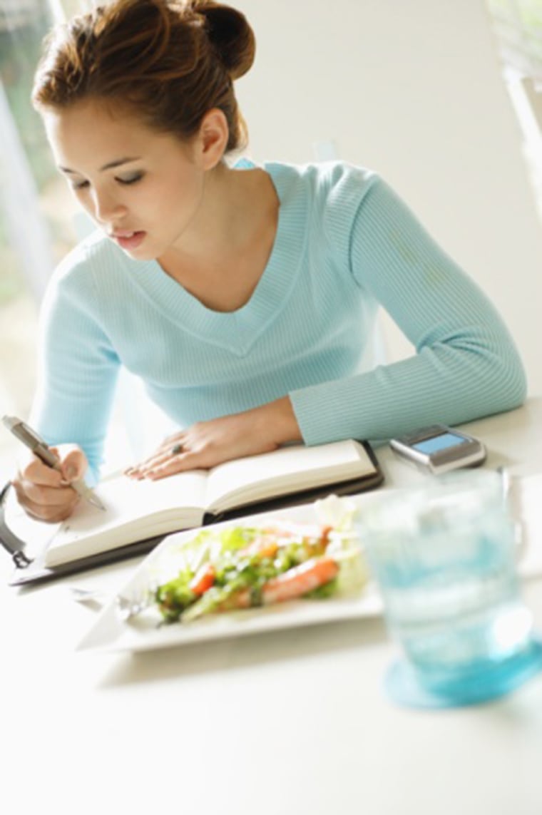Young woman sitting at table, writing in notebook.  Top, Water, Concentration, Table, Food And Drink, Vertical, Waist Up, Indoors, 20-24 Years, Salad,...