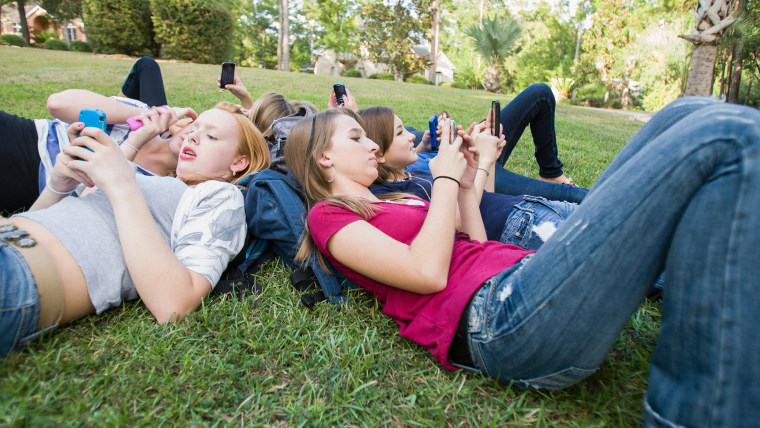 Teen girls text on their phones.