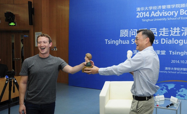 President of Tsinghua's School of Economics and Management, Qian Yingyi, presents a gift to Mark Zuckerberg (L), founder and CEO of Facebook, at Tsing...