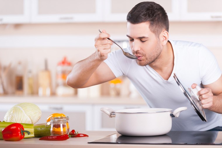 Tasting soup. Handsome young man tasting soup from the pan while standing in the kitchen; Shutterstock ID 187180535; PO: TODAY.com