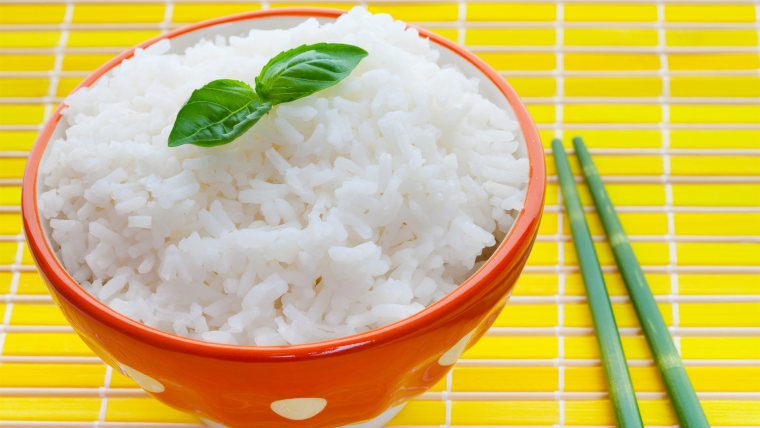 Bowl of steamed rice on yellow with bamboo chopsticks