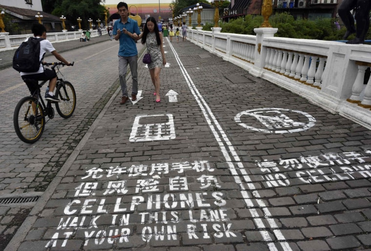 A man rides his bicycle as people walk on the \"first mobile phone sidewalk in China\", which was recently installed at a tourism area in Chongqing muni...