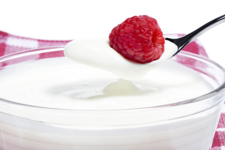 raspberry on a spoon with yogurt over a milk dessert with towel in background and white background