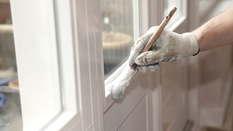 Hand with paintbrush painting a door white; brush; coat; collar; concentrating; concentration; construction; craftsman; detail; diy; do-it-yourself; e...