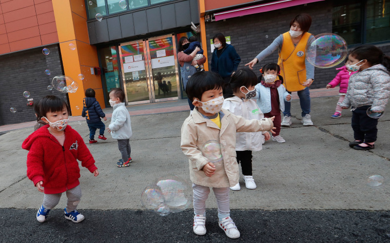 Niños con mascarillas juegan con burbujas de jabón afuera del templo de Chogyesa en Corea del Sur