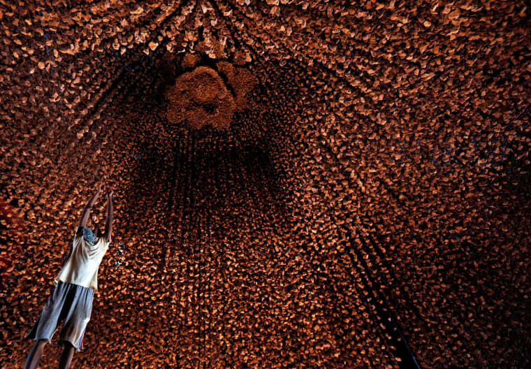 Image: An artisan hangs decorative pieces at a pandal, or a temporary platform, for the upcoming Hindu festival of Durga Puja, in Kolkata