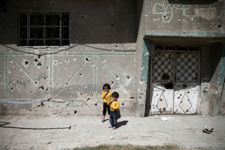 Image: Children stand in front of the bullet-riddled facade of a building in the rebel-held Douma neighbourhood of Damascus
