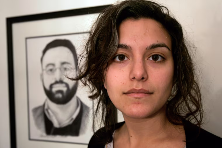 ** ADVANCE FOR MONDAY, MARCH 9 ** Tricia Bhatia, of Medway, Mass., stands in front of a drawing of her brother Michael Bhatia at the family home, in Medway, Thursday, Dec. 4, 2008. Michael Bhatia, an academic, was killed in the area of Khost, Afghanistan, in May of 2008 while working for the Human Terrain System program.  (AP Photo/Steven Senne)