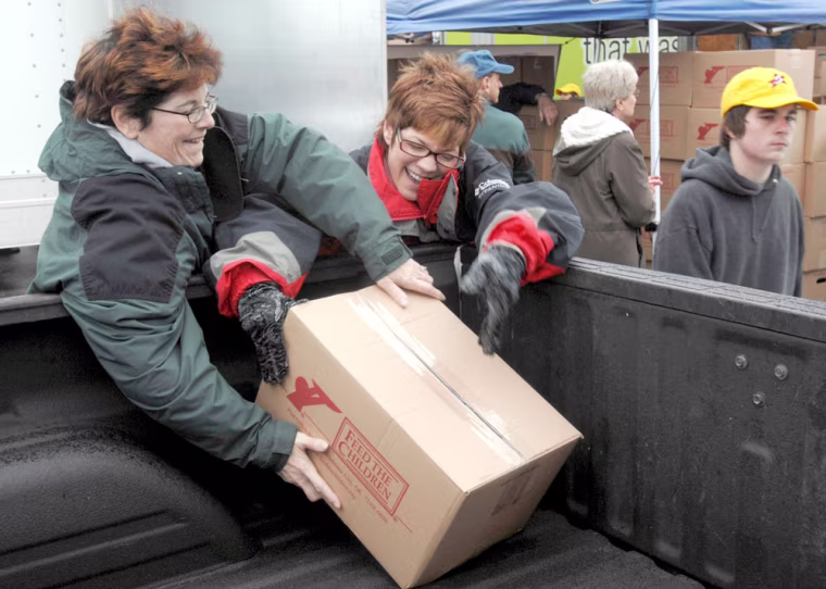 Truth Photo By J. Tyler Klassen Patti Elliott (left) and Kim Anglemire put a food box in the back of a truck at the Feed the Children food drop Tuesday at Concord Mall. The two were part of a large volunteer group that distributed food to about 5000 families.