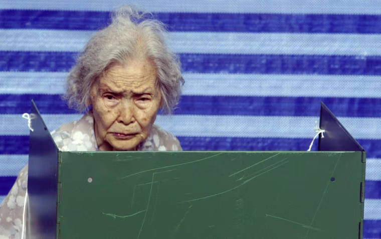 Image: A Thai woman writes names of candidates at a booth before casting vote at a polling station in Bangkok
