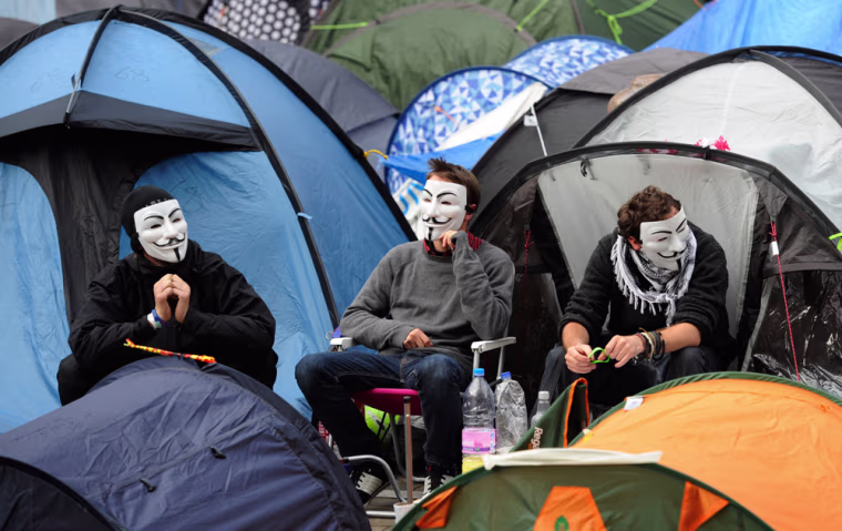 Image: Demonstrators wearing Vendetta masks sit outside tents at the Occupy London camp outside St. Paul's Cathedral.