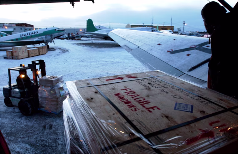 In the predawn hours, Buffalo Airways employees load a crate of windows destined for settlements up the MacKenzie River valley. The airline regularly flies these \"food mail\" runs, so known because the cost of shipping food and supplies is offset by the postal service.