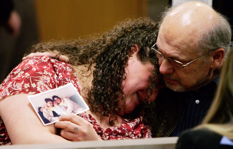 Charlene Kafoury, holding a photo of herself with her mother, is consoled by an unidentified person  in a courtroom as Anthony LaCalamita III, not shown,  the man accused of killing  Kafoury's mother, is arraigned on murder and other charges in District Court in Troy, Mich., Wednesday, April 11, 2007. LaCalamita, a recently fired accountant, is accused of killing a former co-worker and wounding two others during a shotgun attack at the office building in which he previously worked. (AP Photo/Carlos Osorio)